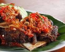 Gambar Iga Penyet at Warung Iga Penyet Bu Parmi Solo, crushed with sambal and served with fresh vegetables.