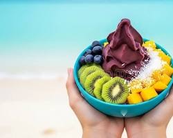 hand holding a colorful acai bowl against a blurred beach backgroundの画像