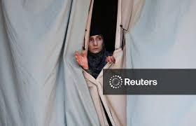 A Kashmiri woman looks through a window covered with a plastic sheet after finishing noon prayers on the first day of the holy fasting month of Ramadan at Jamia Masjid in Srinagar