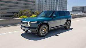 A white Rivian R2 electric vehicle parked on a scenic road