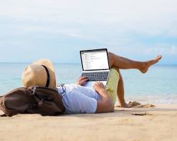 Image of person relaxing on a beach with a drink and a laptop, symbolizing financial relaxation