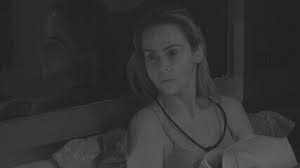 Mulher loira com olhar apreensivo em ambiente escuro, possivelmente em um reality show.