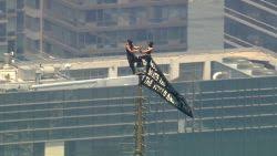 Two people scale to the top of the Empire State Building holding banner