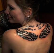Bold black angel wings on upper back with lettering flowing in style above it. wings on upper back tattoo 30 Magnificent Upper Back Tattoos - wings-on-upper-back-tattoo