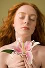 Young woman holding flower (Stargazer Lily), eyes closed, head and shoulders. By: PM Images. Iconica - 200566005-009