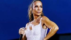 Ivete Sangalo em show com vestido branco brilhante e cabelo preso em rabo de cavalo, com fundo azul.