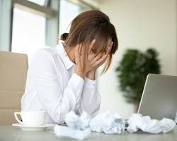 Image of person sitting at a laptop, looking stressed and surrounded by coffee cups and crumpled paper