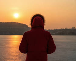 person wearing a light jacket looking at the sea in winterの画像