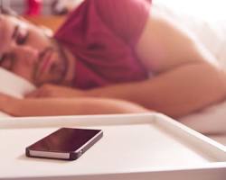 Persona durmiendo en una cama con un teléfono móvil apagado en la mesita de noche, representando la importancia de desconectar de las pantallas antes de dormir para mejorar la calidad del sueño y el bienestar digital.