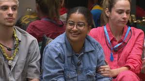 Três participantes do BBB 23 sentados, com destaque para a participante Sarah Aline sorrindo.