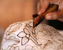 Gambar Seorang pengrajin batik sedang melukis batik tulis dengan canting