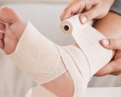 Image of person using a bandage roller to apply a bandage to their ankle