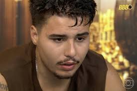 Participante do BBB 23, Gabriel Santana, em close-up, com expressão pensativa. Ao fundo, elementos decorativos e logo do BBB.